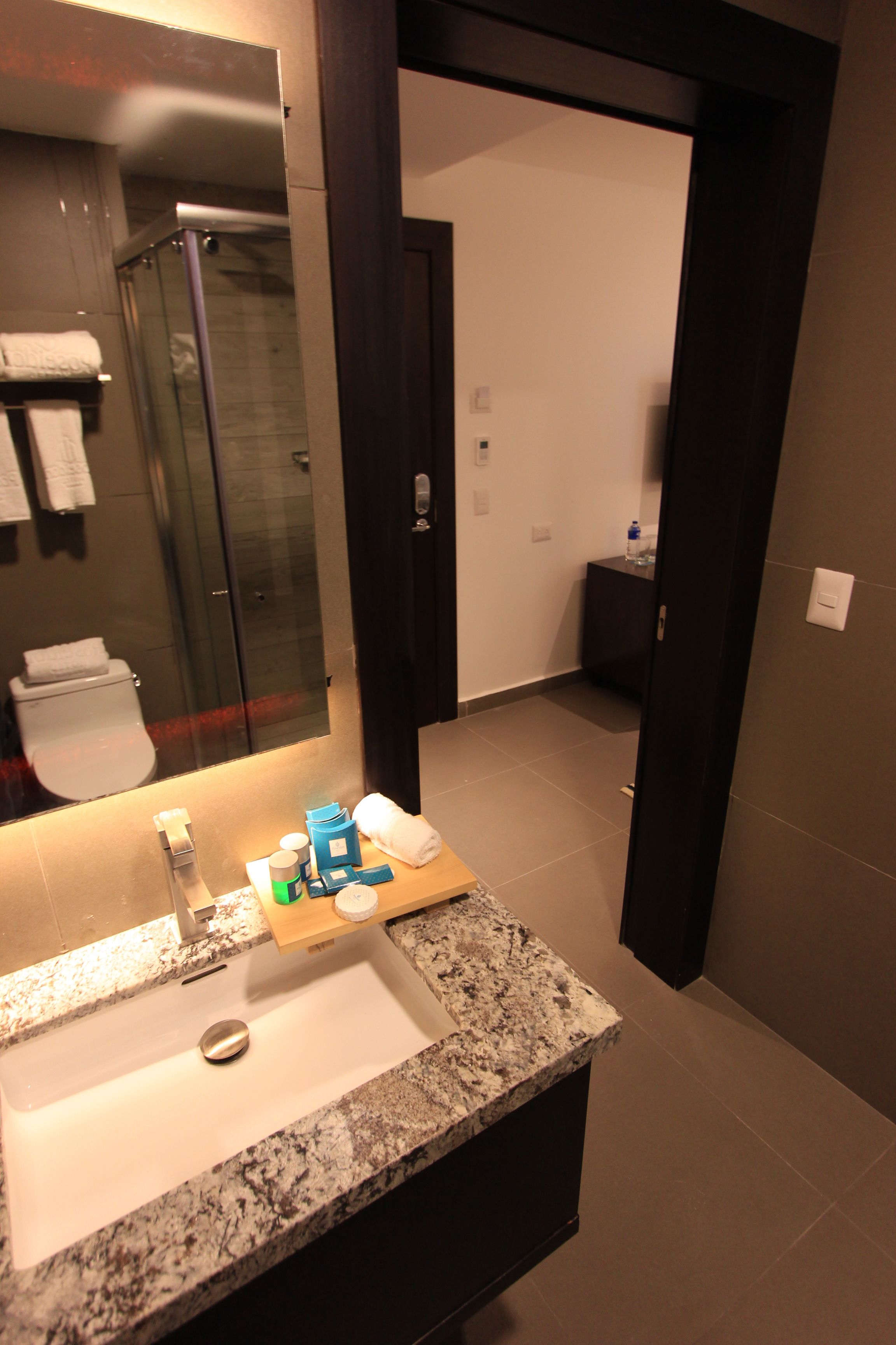 Een moderne badkamer met een granieten aanrechtblad, een spiegel en een zichtbare douche.