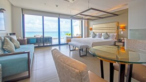 Une chambre d’hôtel moderne dotée d’un grand balcon, d’un lit, d’un canapé, d’une table en verre et offrant une vue sur l’océan.
