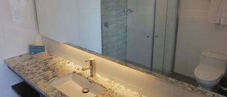 Un baño moderno con encimera de mármol, lavamanos, cabina de ducha de vidrio e inodoro.