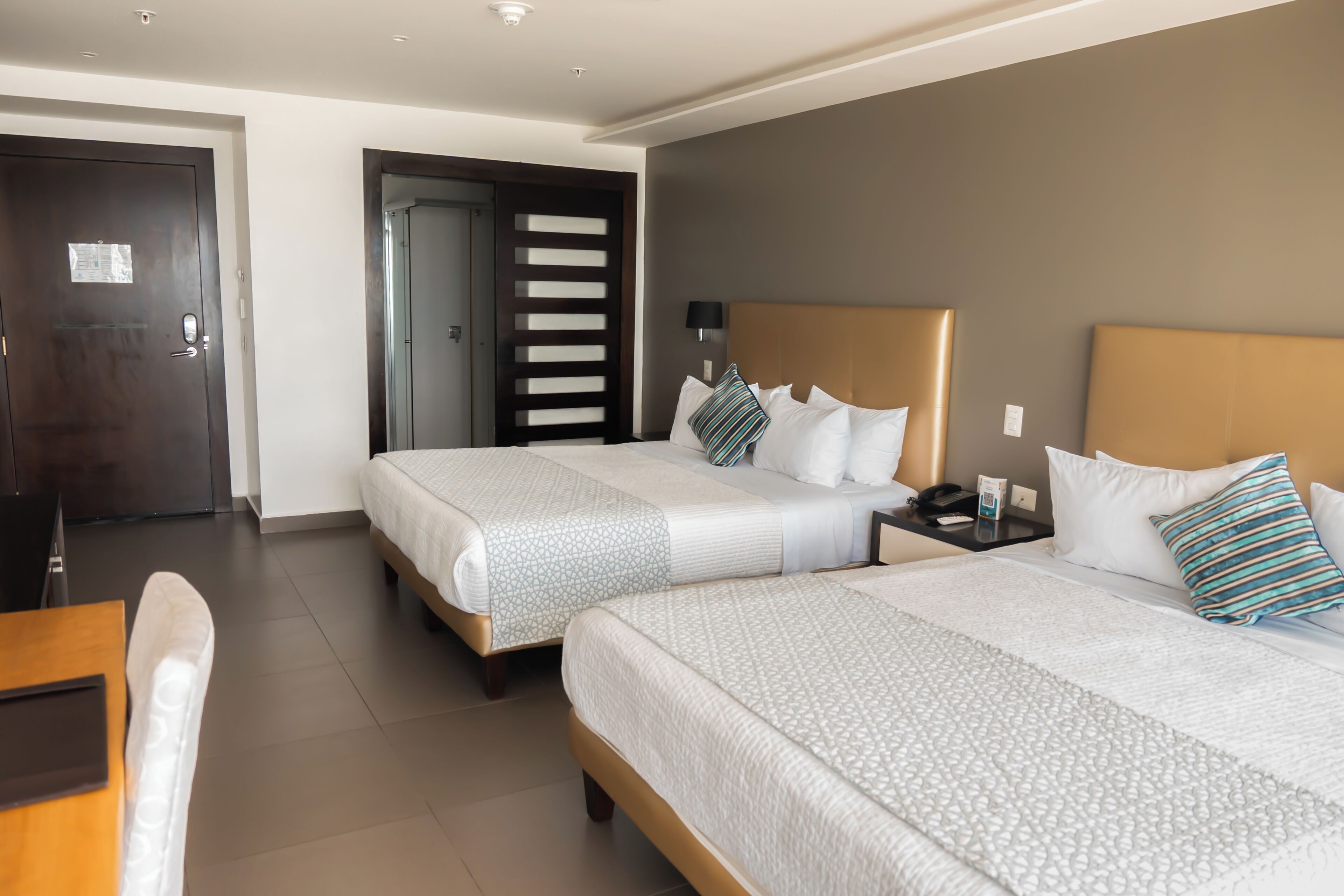 A hotel room with two beds, a wooden desk, and a door.