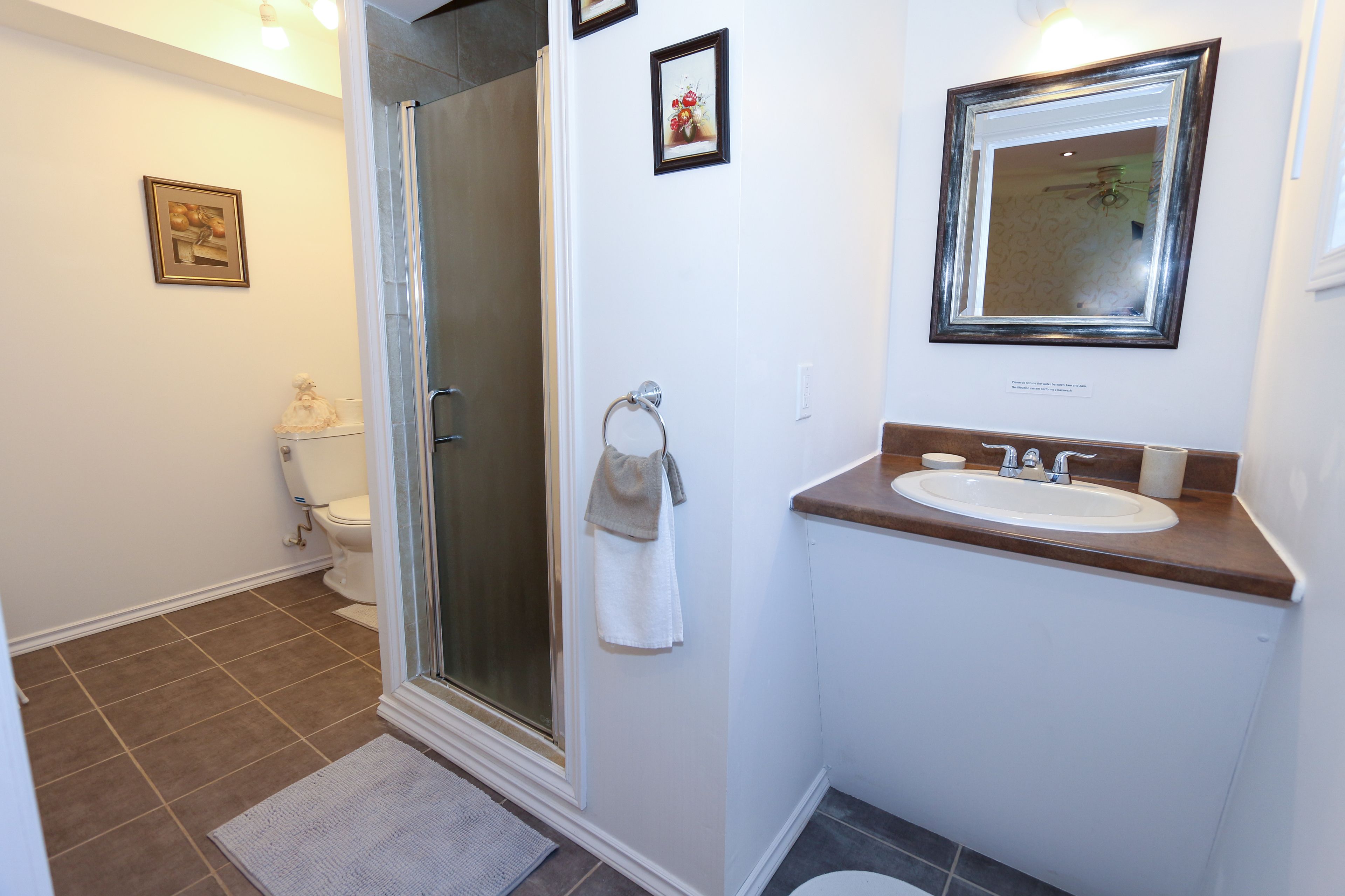 A bathroom with a shower, toilet, sink, and a framed mirror.