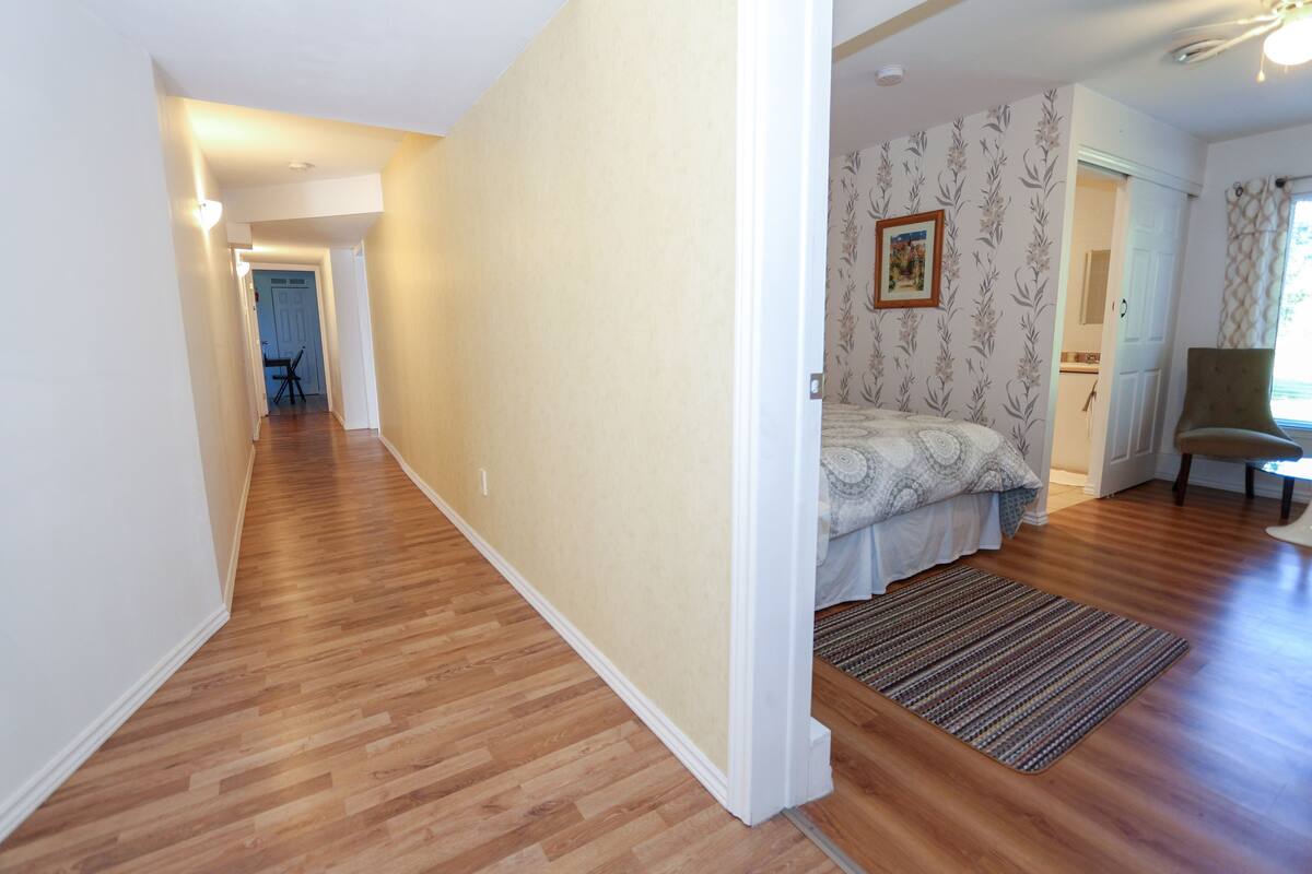 A hallway with wooden flooring, a bed with patterned bedding, a chair, and a door leading to another room.