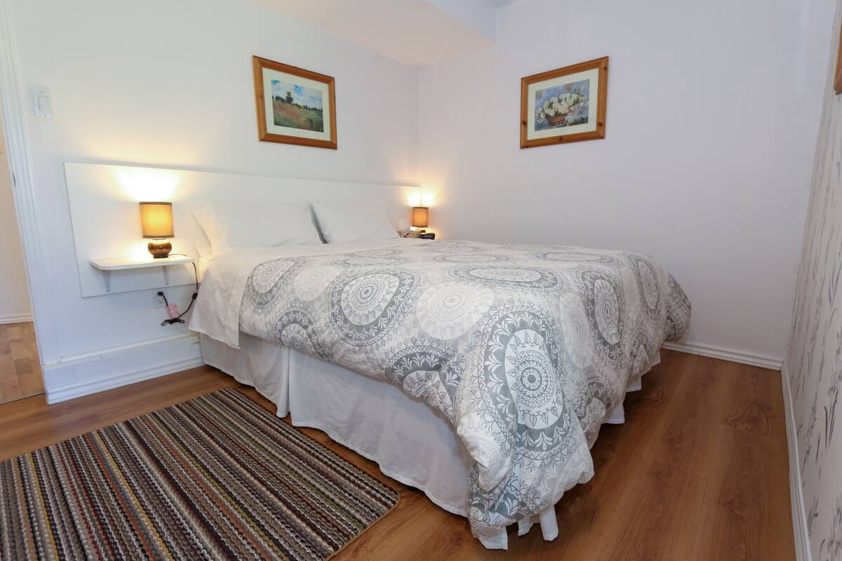 A bedroom with a large bed, two bedside tables with lamps, a patterned bedspread, and two framed pictures on the wall.