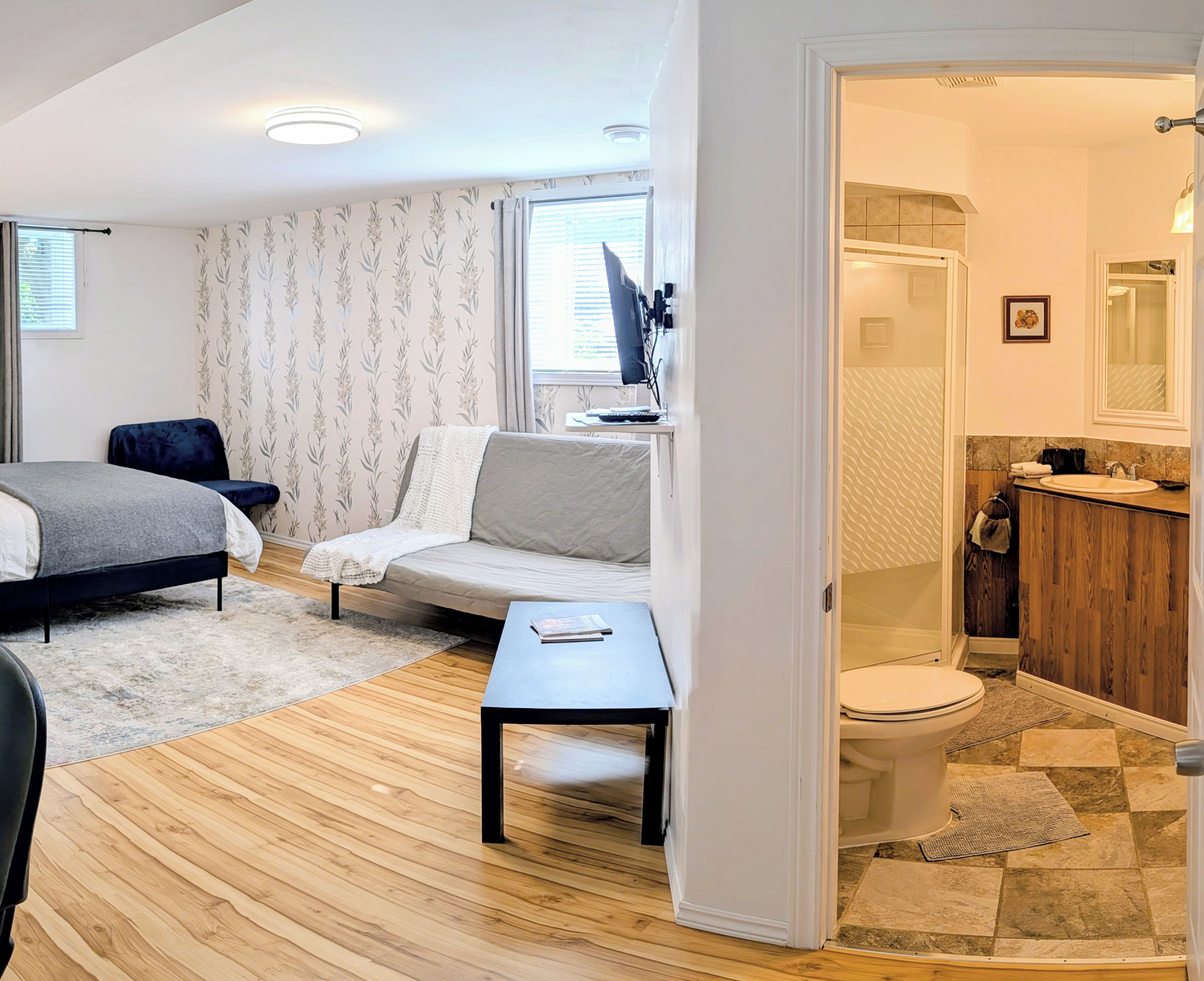 A modern bedroom with a bed, a sofa, a small table, and a bathroom with a toilet and sink.
