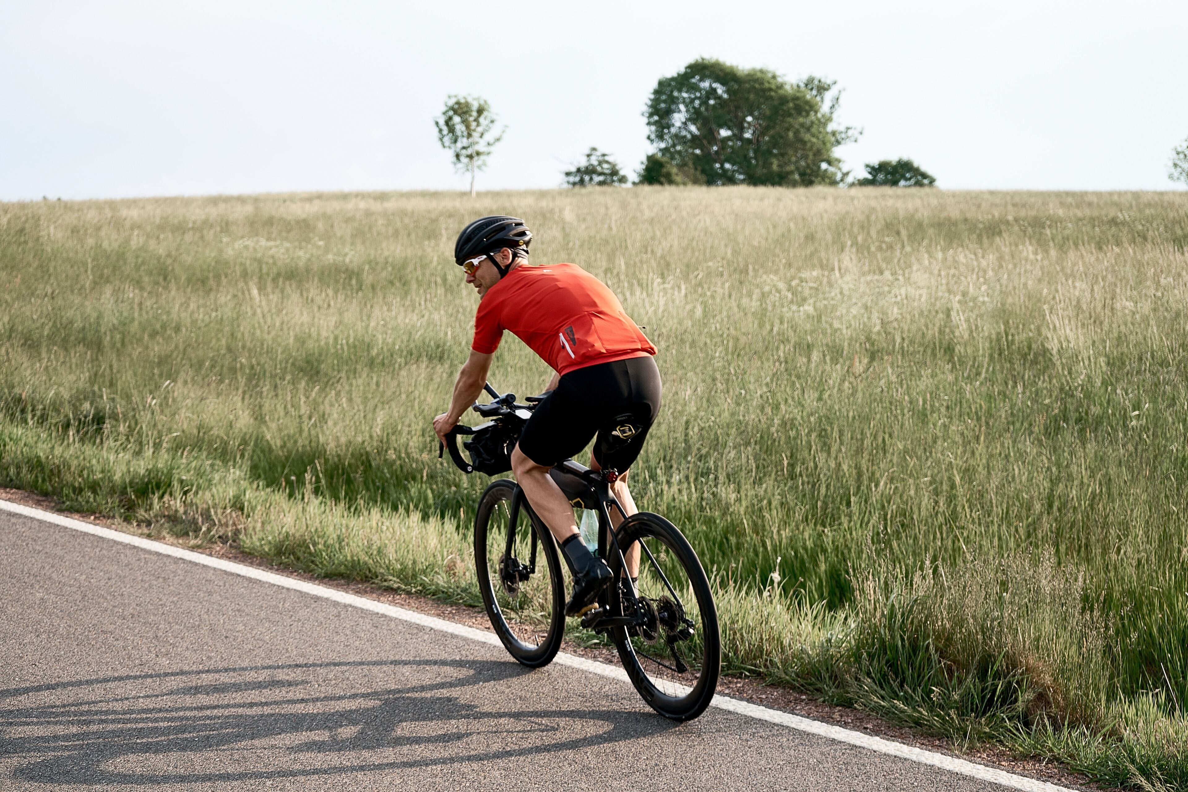 A cyclist riding a bicycle on a road with grassy fields on both sides.