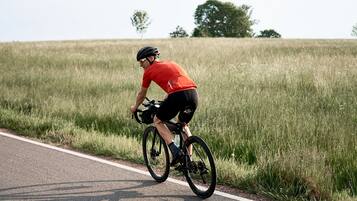 A cyclist riding a bicycle on a road with grassy fields on both sides.
