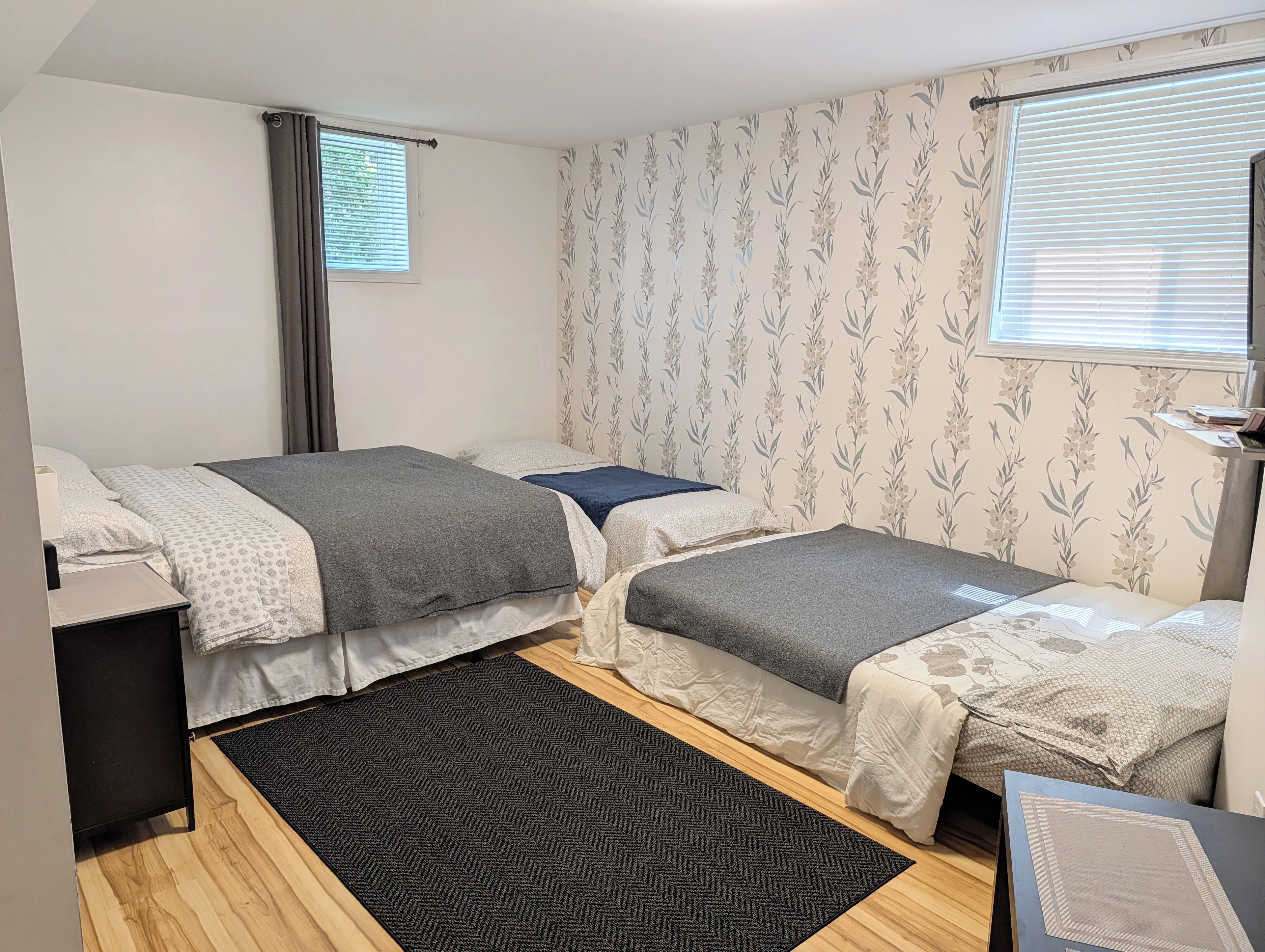 Un dormitorio con dos camas, un escritorio pequeño, una ventana con persianas y un papel tapiz estampado.
