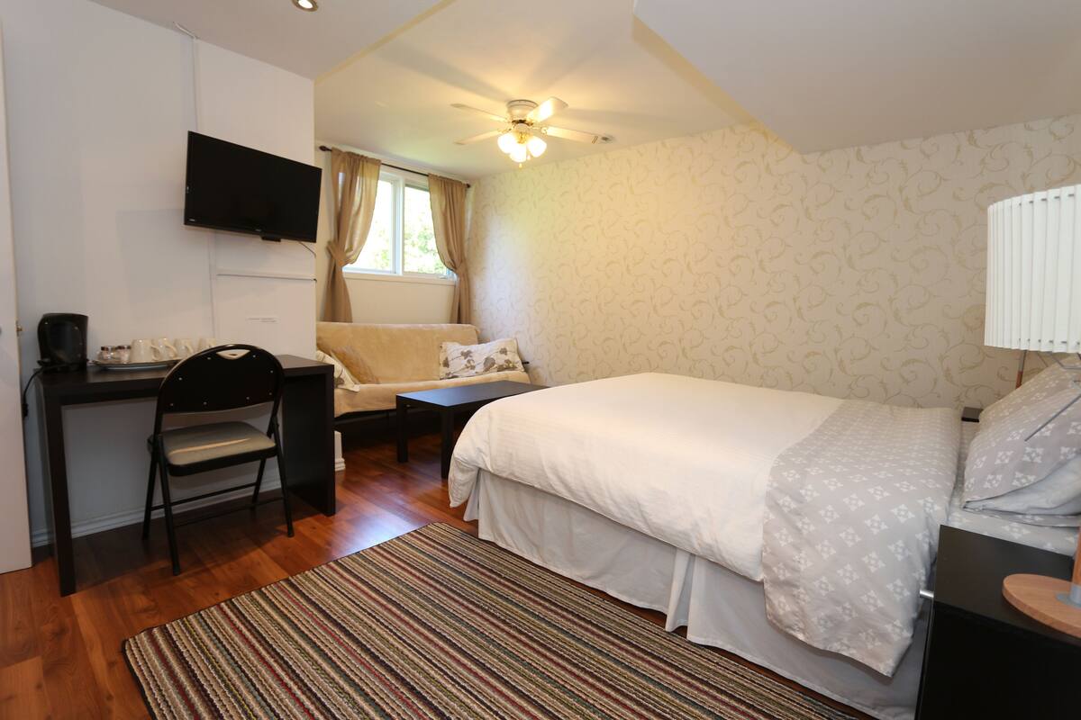 A bedroom with a bed, a desk, a chair, a TV, and a window with curtains.