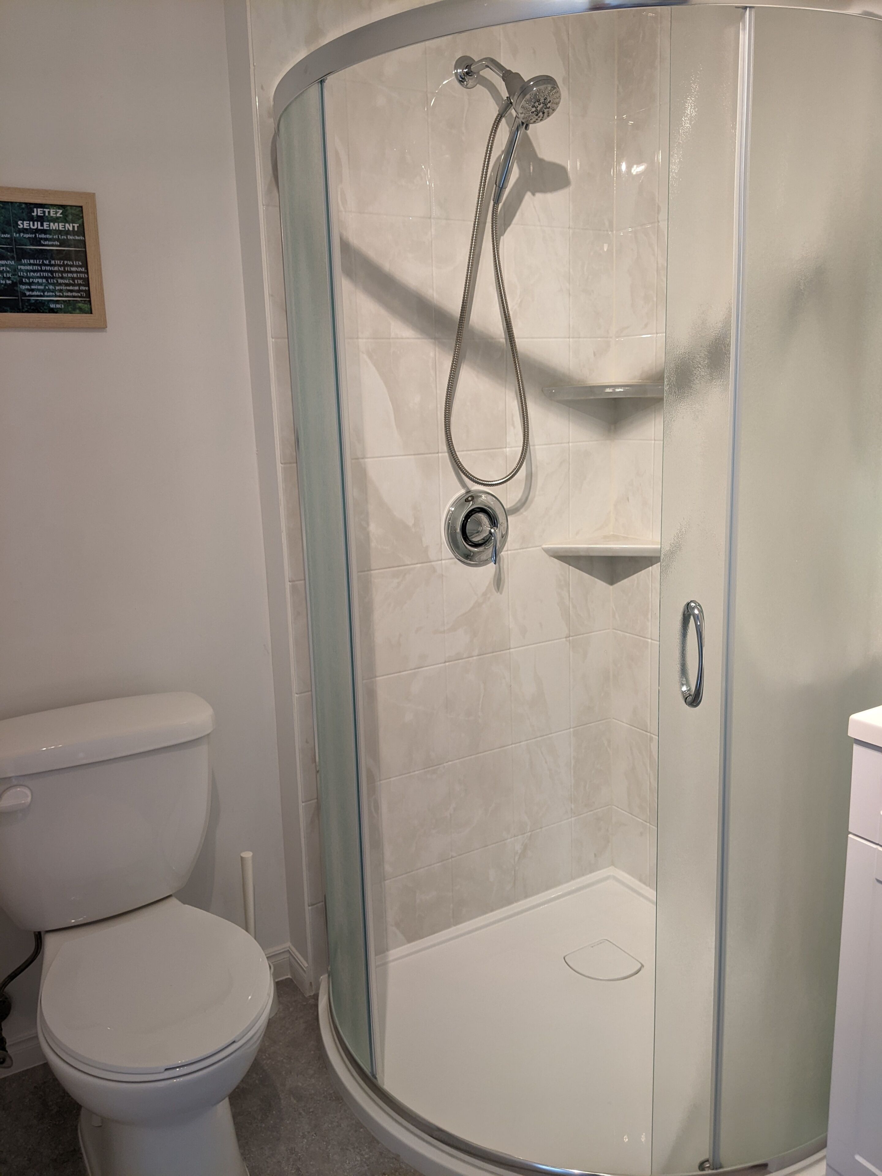 Une douche fermée par des parois en verre, dotée d’un pommeau de douche à main et d’un robinet mural.