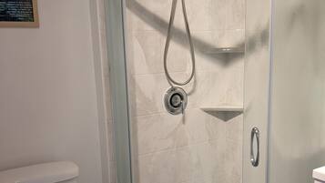 Une douche fermée par des parois en verre, dotée d’un pommeau de douche à main et d’un robinet mural.