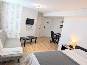 A hotel room with a bed, a desk with a chair, a television on the wall, and a door. - Cedar Drive Inn (North Stormont)
