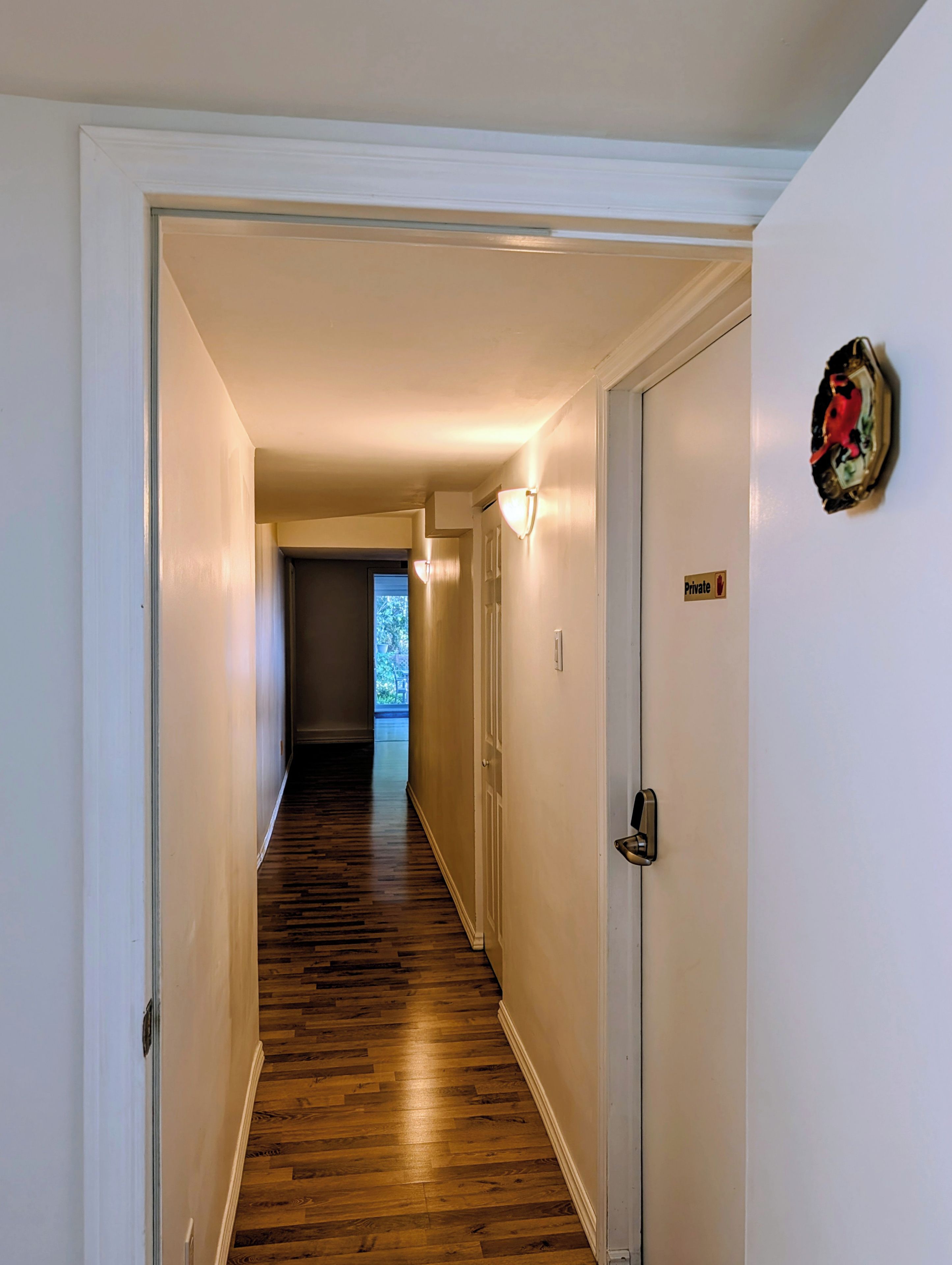 A hallway with a wooden floor, white walls, and a door with a 'Private' sign.