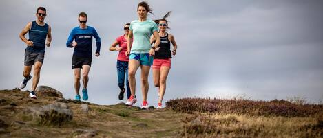 A group of people running on a grassy hill with a cloudy sky in the background.