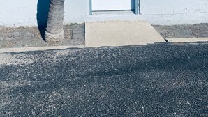 A building with a white door marked with the number 4, a window with a view, and a concrete planter. - Sunset Motel (Alice)