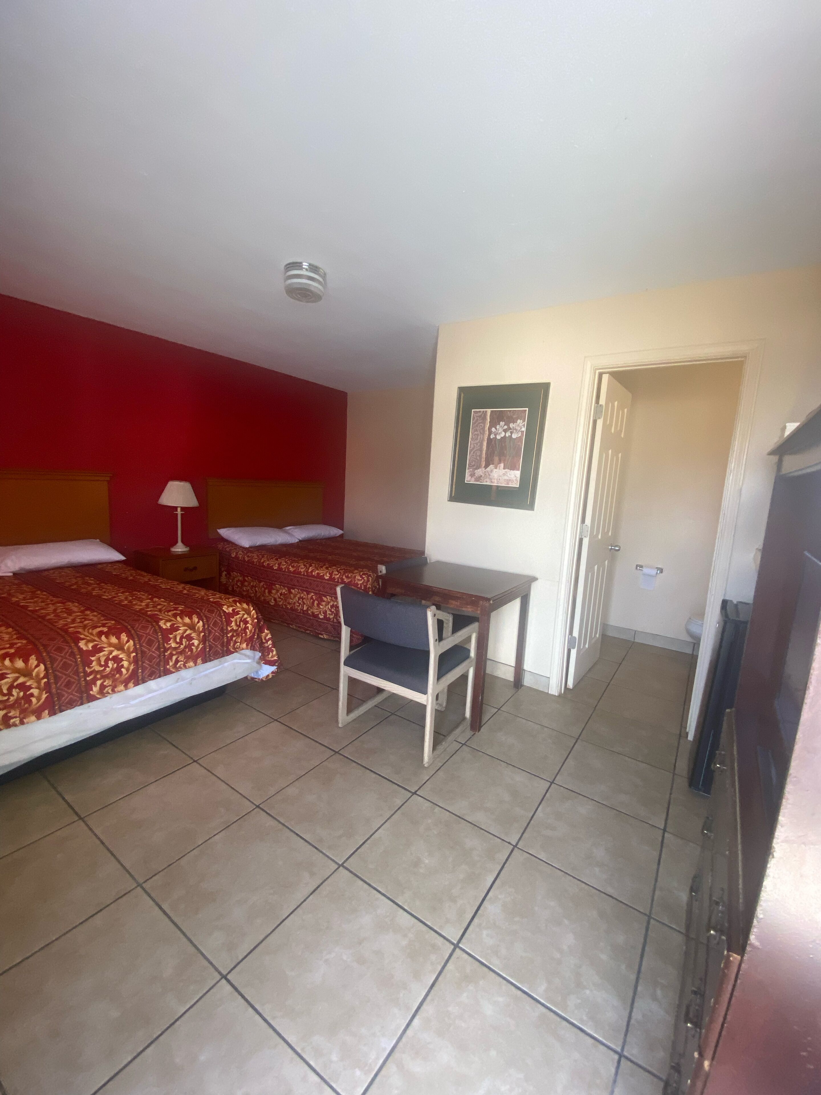 Quarto de hotel com duas camas, uma mesa pequena, uma cadeira e uma televisão.