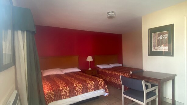 A hotel room with two beds, a desk, and a chair. - Sunset Motel (Alice)