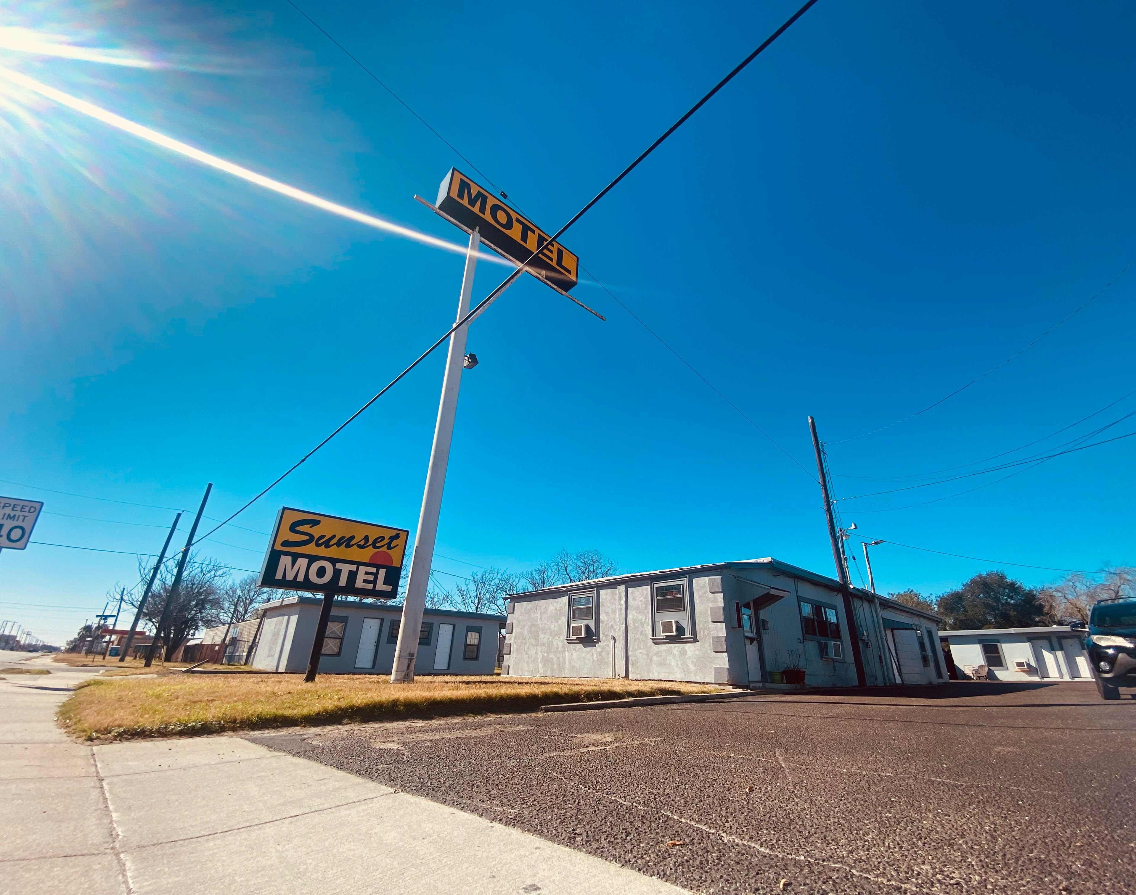 A motel with a 'Sunset Motel' sign, a speed limit sign, and a clear blue sky.