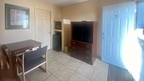 A room with a dining table, chairs, a television, a microwave, and a door. - Sunset Motel (Alice)