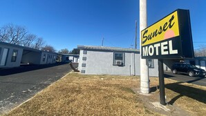 A motel sign with the name 'Sunset Motel' and a small building with a gray exterior. - Sunset Motel (Alice)