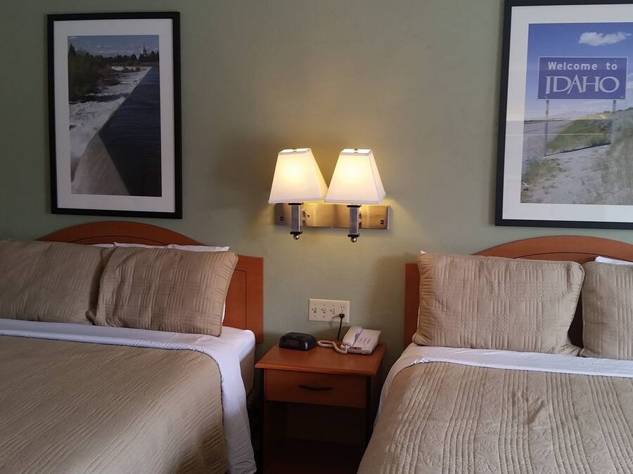 Habitación de hotel con dos camas, una mesita de noche con teléfono y lámpara, y cuadros en la pared.