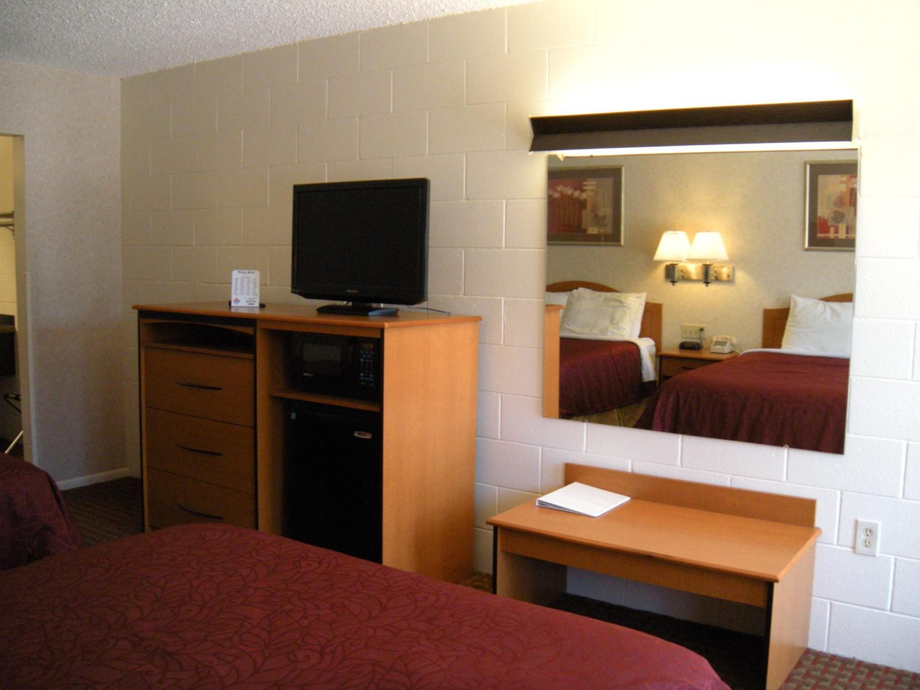 Una habitación de hotel con cama, escritorio, televisor y espejo.