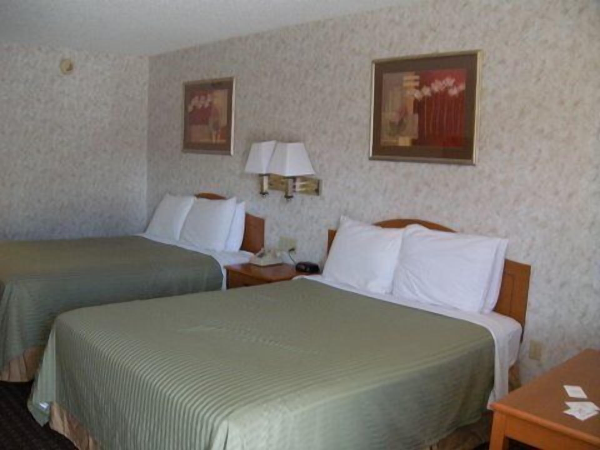 A hotel room with two single beds, a nightstand, a lamp, and two framed pictures on the wall.