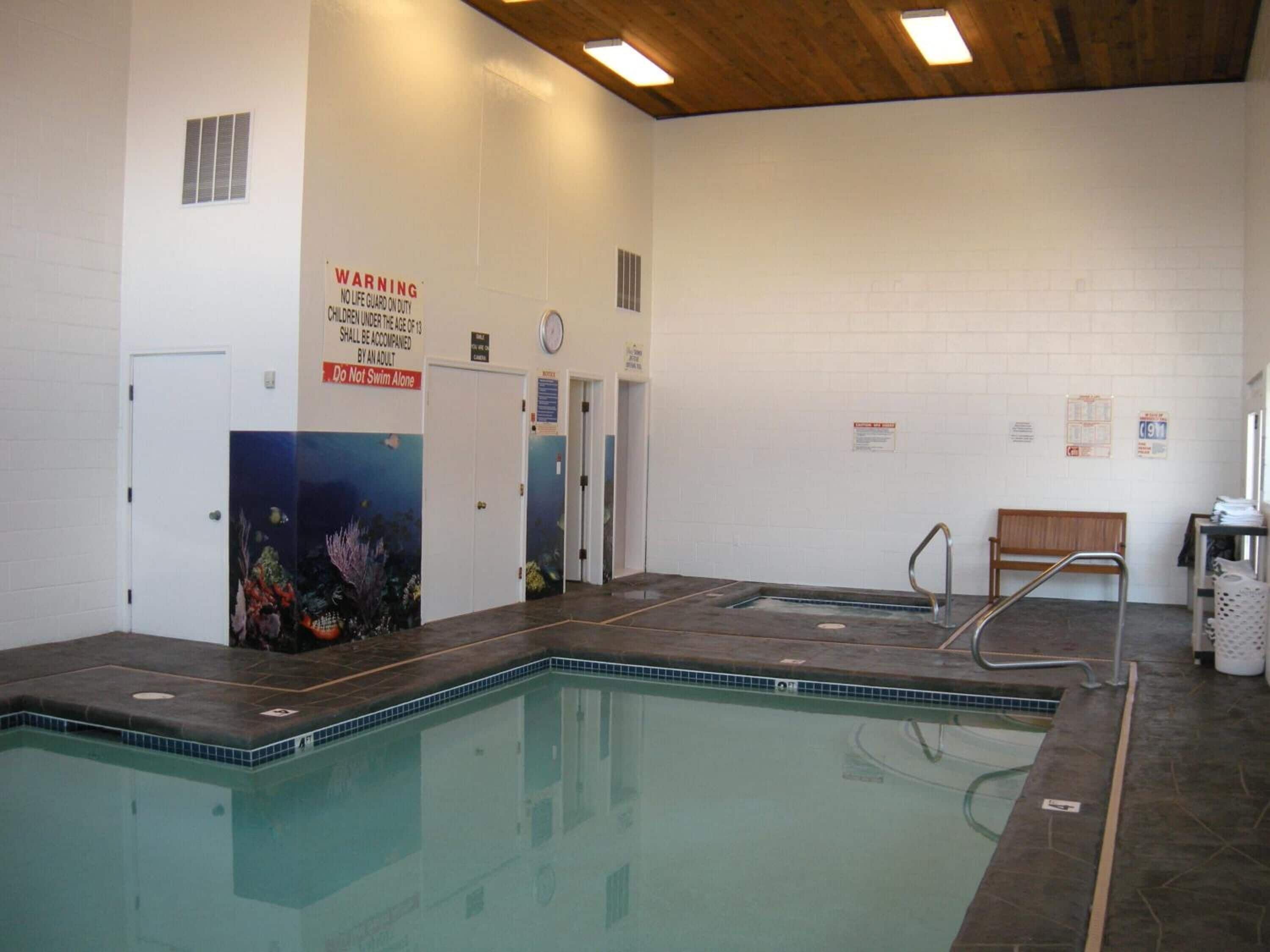 An indoor swimming pool with a warning sign, a bench, and a clock on the wall.