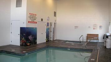 An indoor swimming pool with a warning sign, a bench, and a clock on the wall.