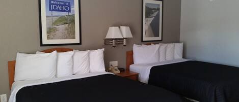 A hotel room with two beds, a nightstand with a lamp, a phone, and framed pictures on the wall.