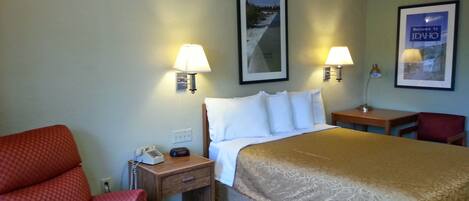 A hotel room with a bed, two bedside lamps, a desk with a chair, a telephone, and a framed welcome sign.
