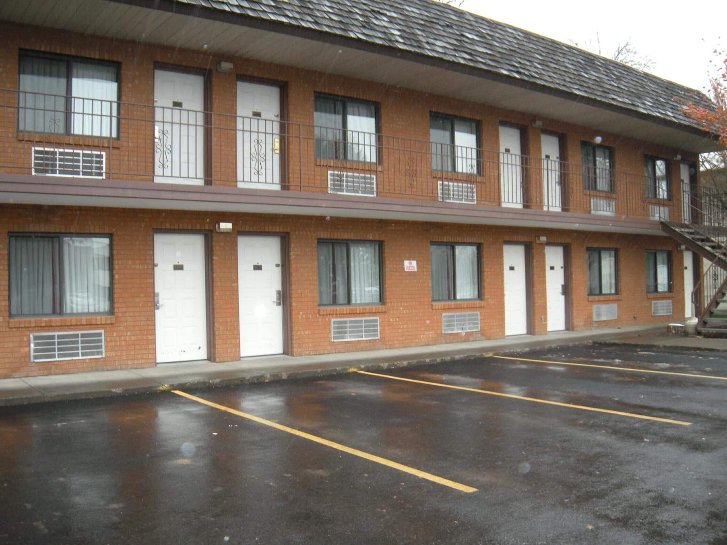 A two-story motel with a brick facade, multiple windows, and a parking lot with marked spaces.