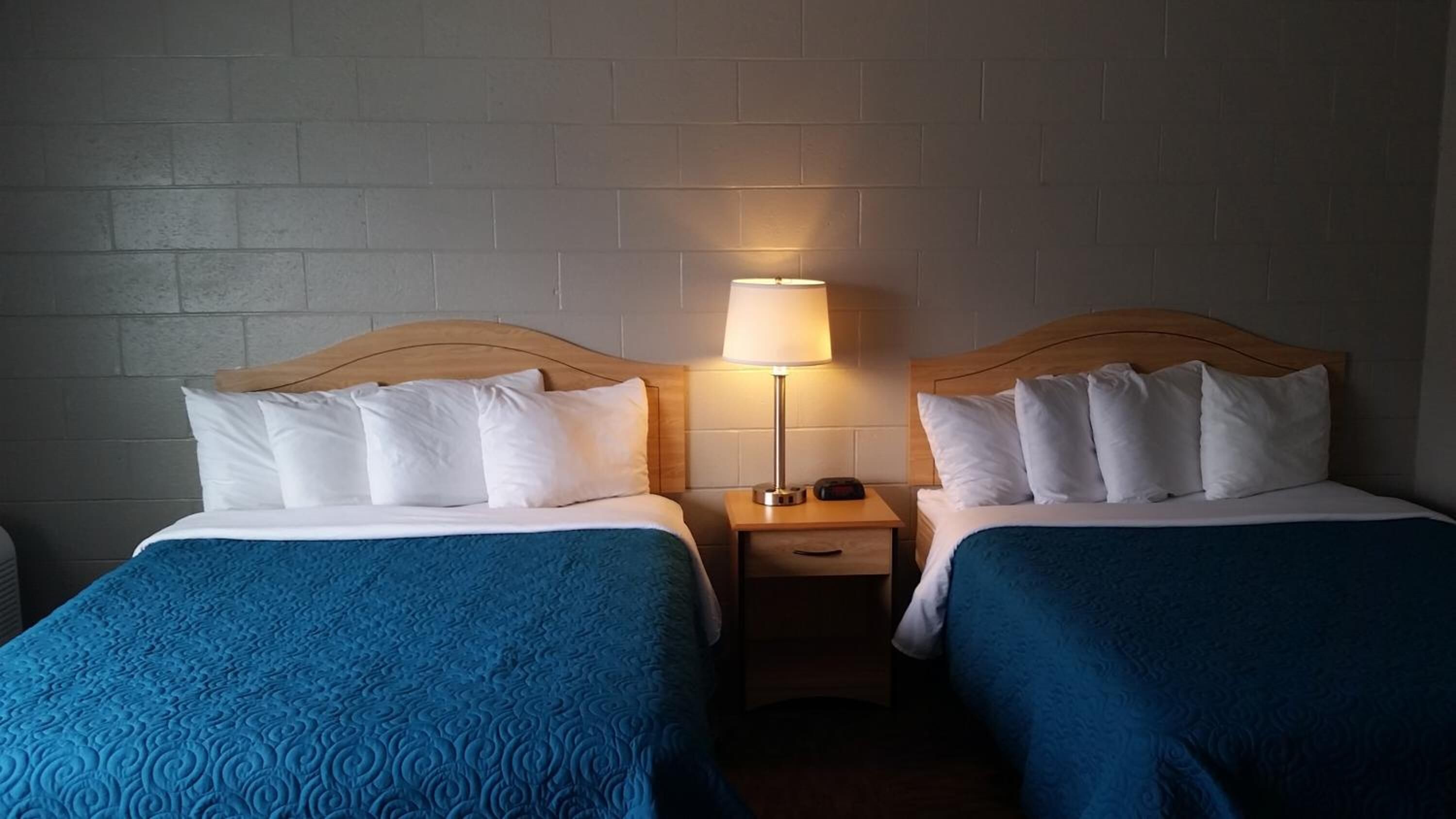 Two single beds with blue bedding, a nightstand with a lamp, and a brick wall.