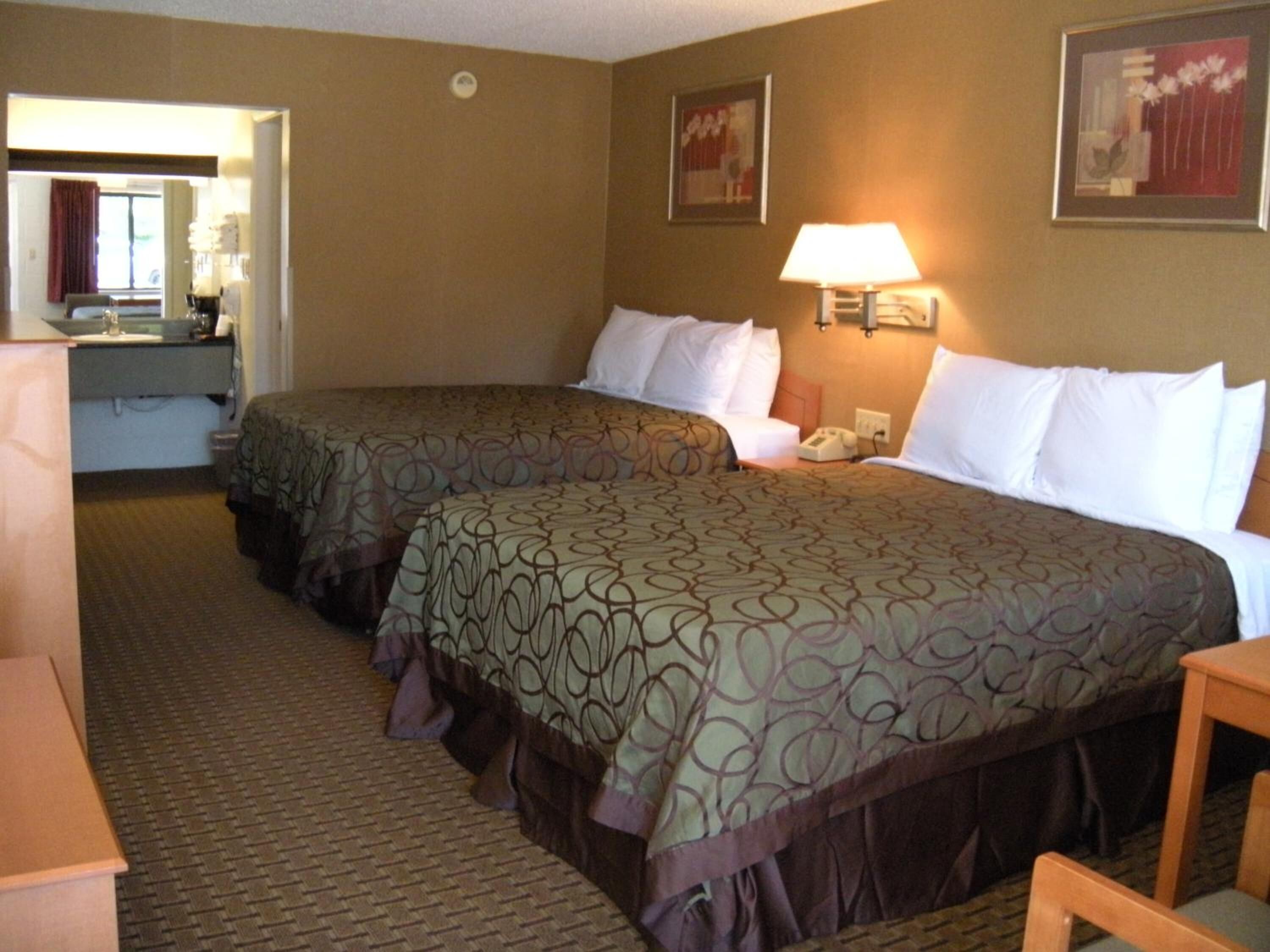 A hotel room with two beds, a desk, a chair, a lamp, and a mirror.