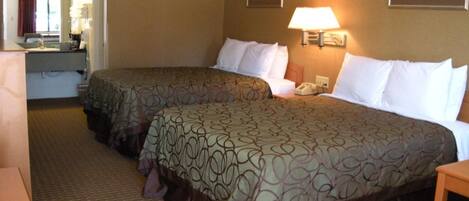 A hotel room with two beds, a desk, a chair, a lamp, and a mirror.