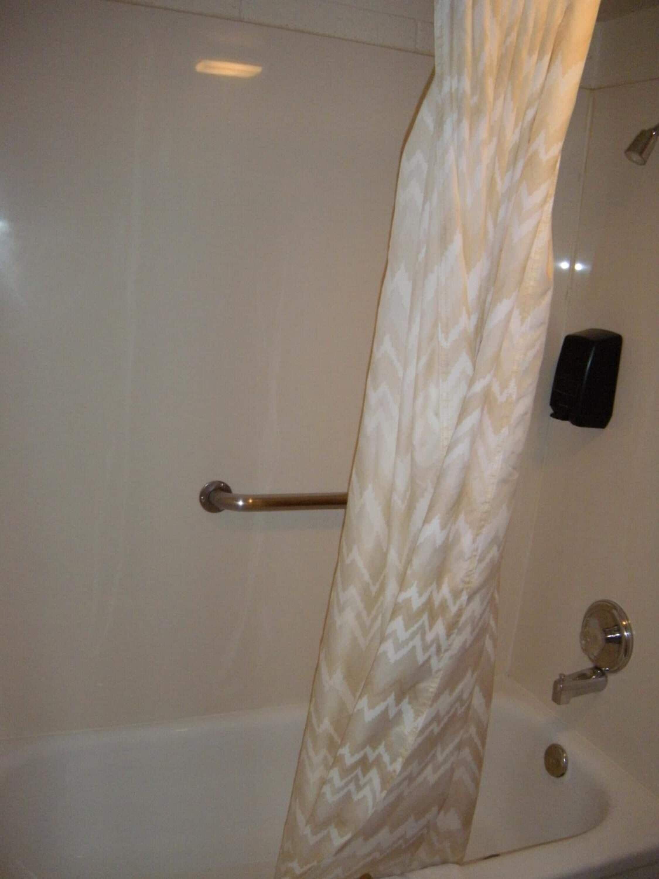 A bathroom with a bathtub, a towel rack, and a soap dispenser.