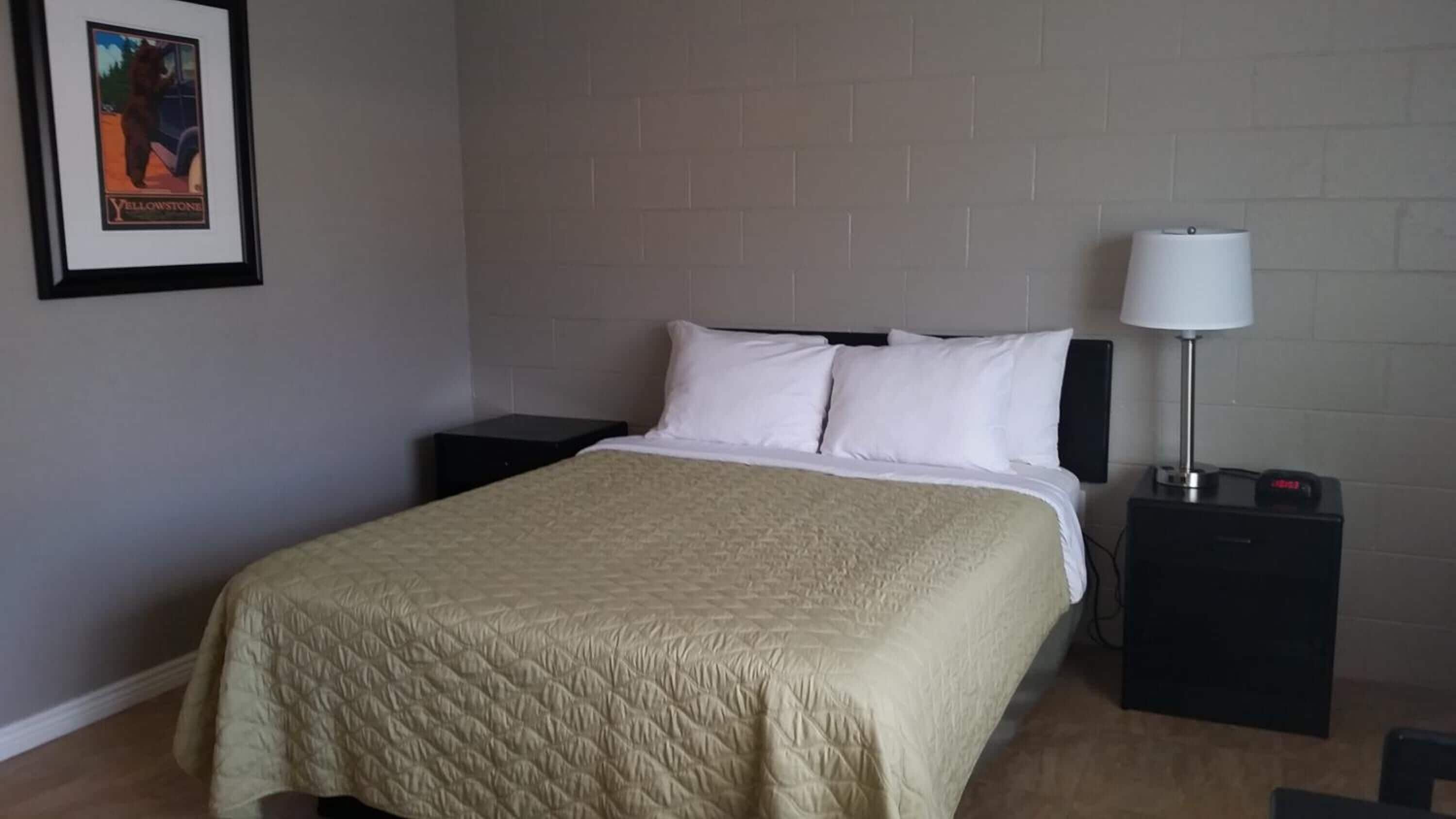 A neatly made bed with a quilted blanket, a bedside lamp, and a framed picture on the wall.