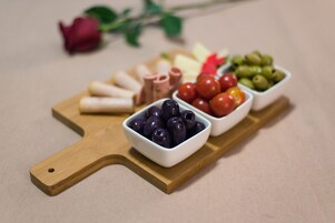 Una tabla de madera con diversos alimentos, entre ellos aceitunas, tomates cherry y lonchas de queso.