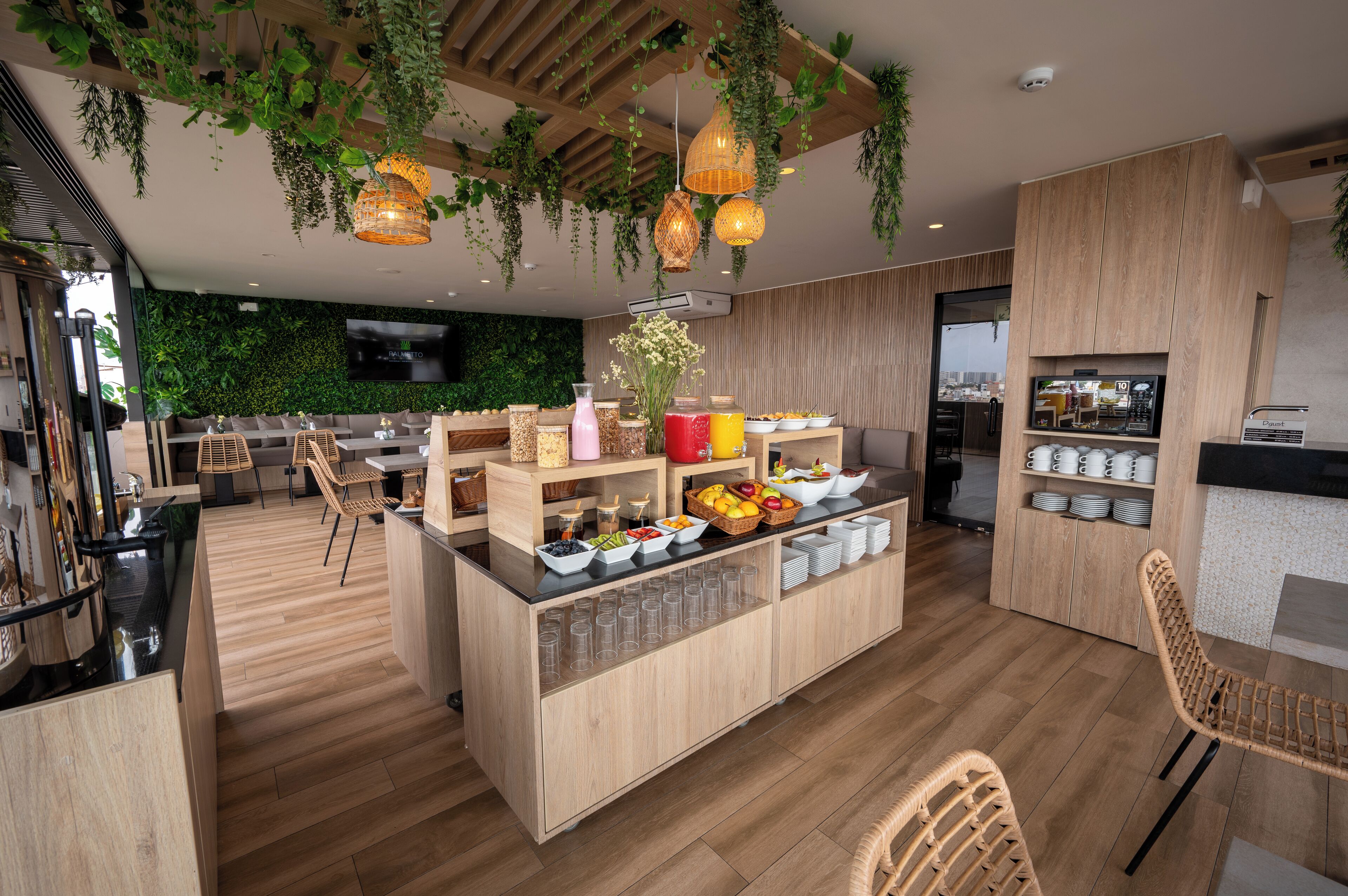 A modern cafe with wooden furniture, a central counter with food and drink options, and hanging plants.