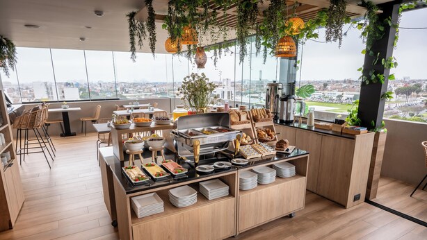 A high-rise restaurant with a buffet setup, wooden flooring, and large windows offering city views. - Palmetto Hotel Business San Miguel (Lima)