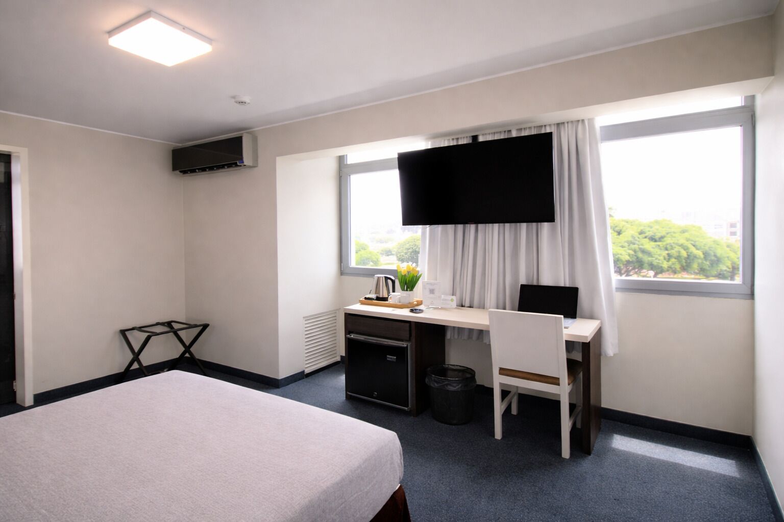 Habitación de hotel con cama, escritorio, silla, televisor y ventanas.