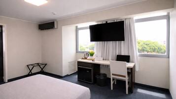 Habitación de hotel con cama, escritorio, silla, televisor y ventanas.