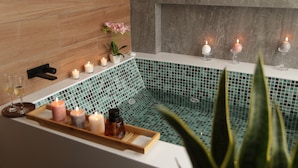 A spa area with a tiled bathtub, candles, and a tray with bottles. - Palmetto Hotel Business San Miguel (Lima)