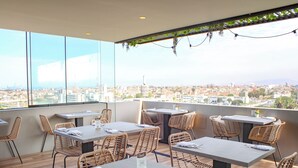 A rooftop restaurant with tables and wicker chairs, overlooking a cityscape. - Palmetto Hotel Business San Miguel (Lima)
