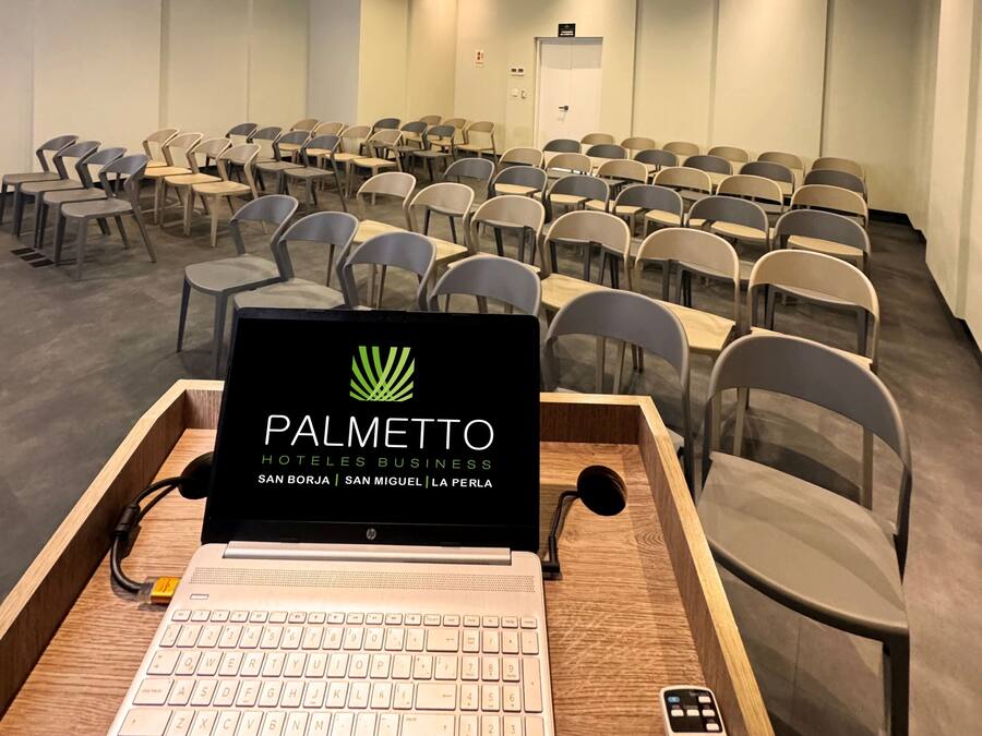 A conference room with rows of chairs, a laptop on a wooden table, and a ceiling with recessed lighting.