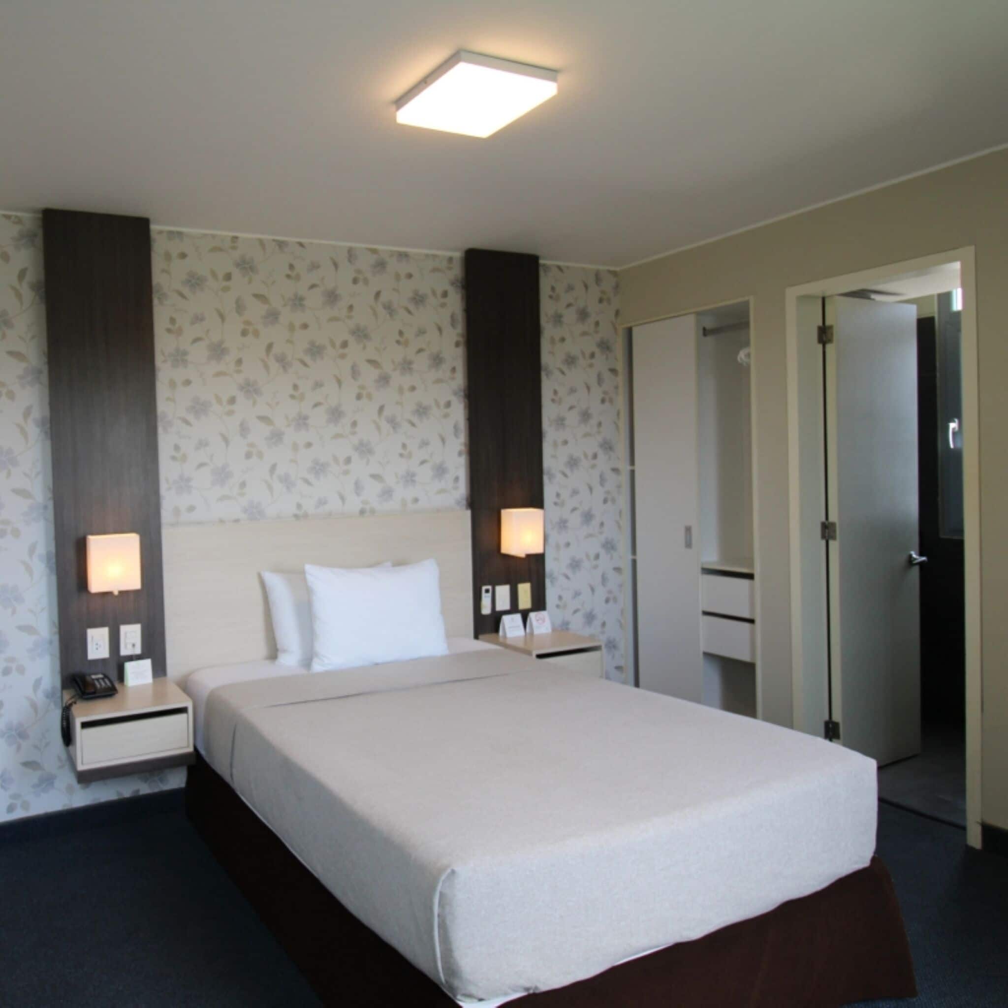 A hotel room with a bed, nightstands, a mirror, and a door.