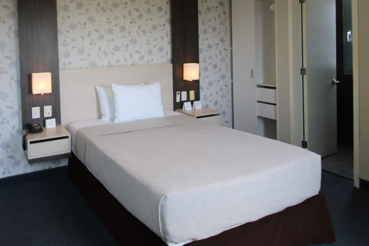 A hotel room with a bed, nightstands, a mirror, and a door.