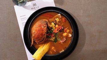 Un bol de soupe contenant un gros morceau de viande, des légumes et une garniture, le tout servi dans une assiette noire.