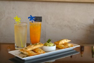 Uma mesa com duas bebidas, um prato de pastelaria e uma pequena tigela de molho.