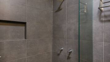 A modern shower area with dark tiles, a glass partition, and a metal towel rack.