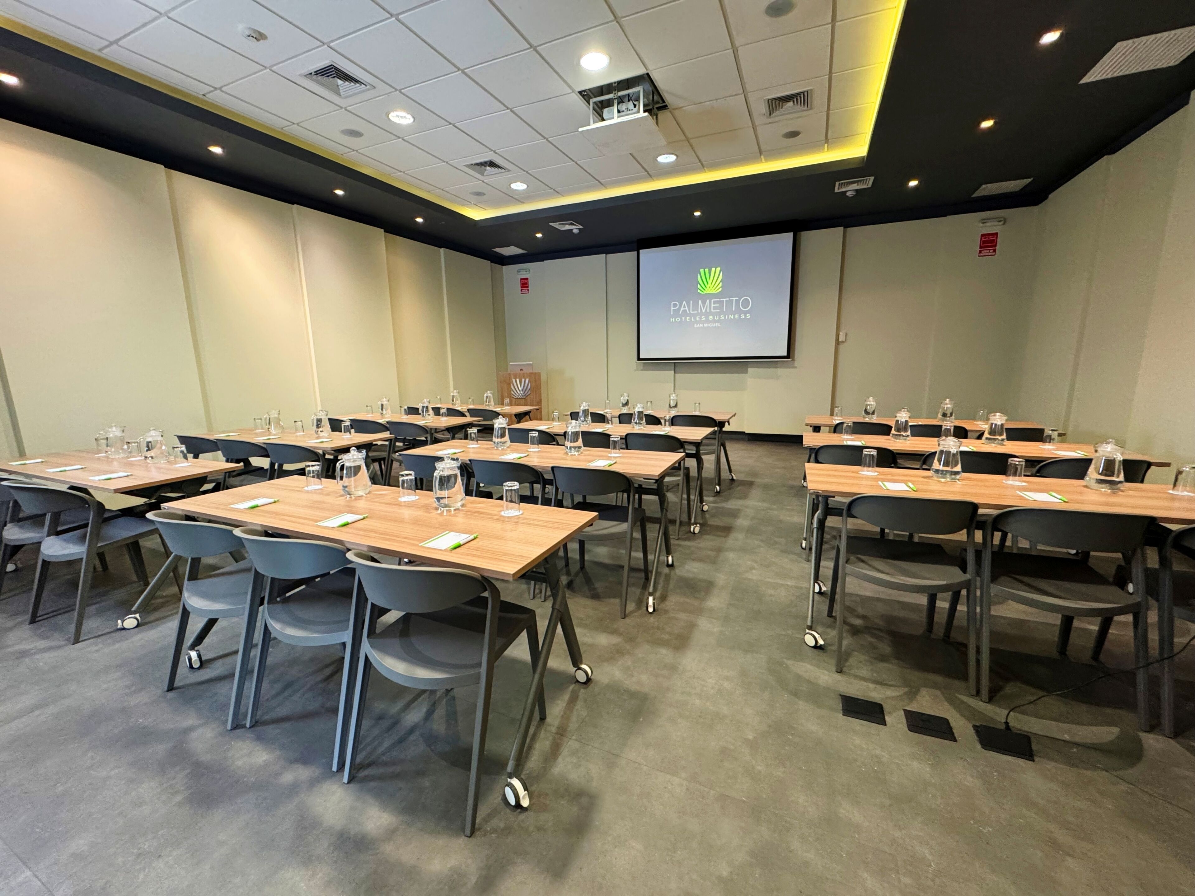 A conference room with tables, chairs, and a projector screen displaying the logo of 'PALMETTO Hotels Business.'